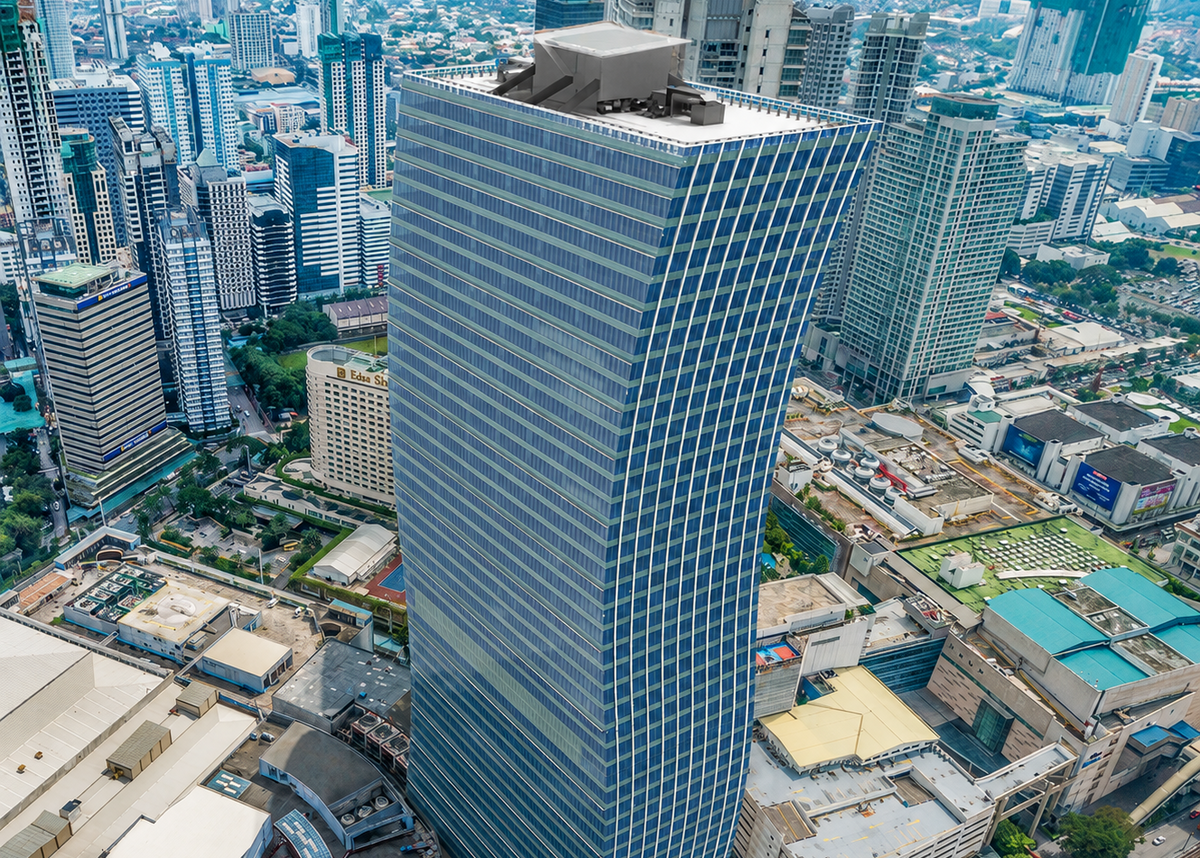 An aerial view of a tall modern glass skyscraper with a curved, tapered design, situated in a dense urban city environment with surrounding buildings, roads, and greenery.