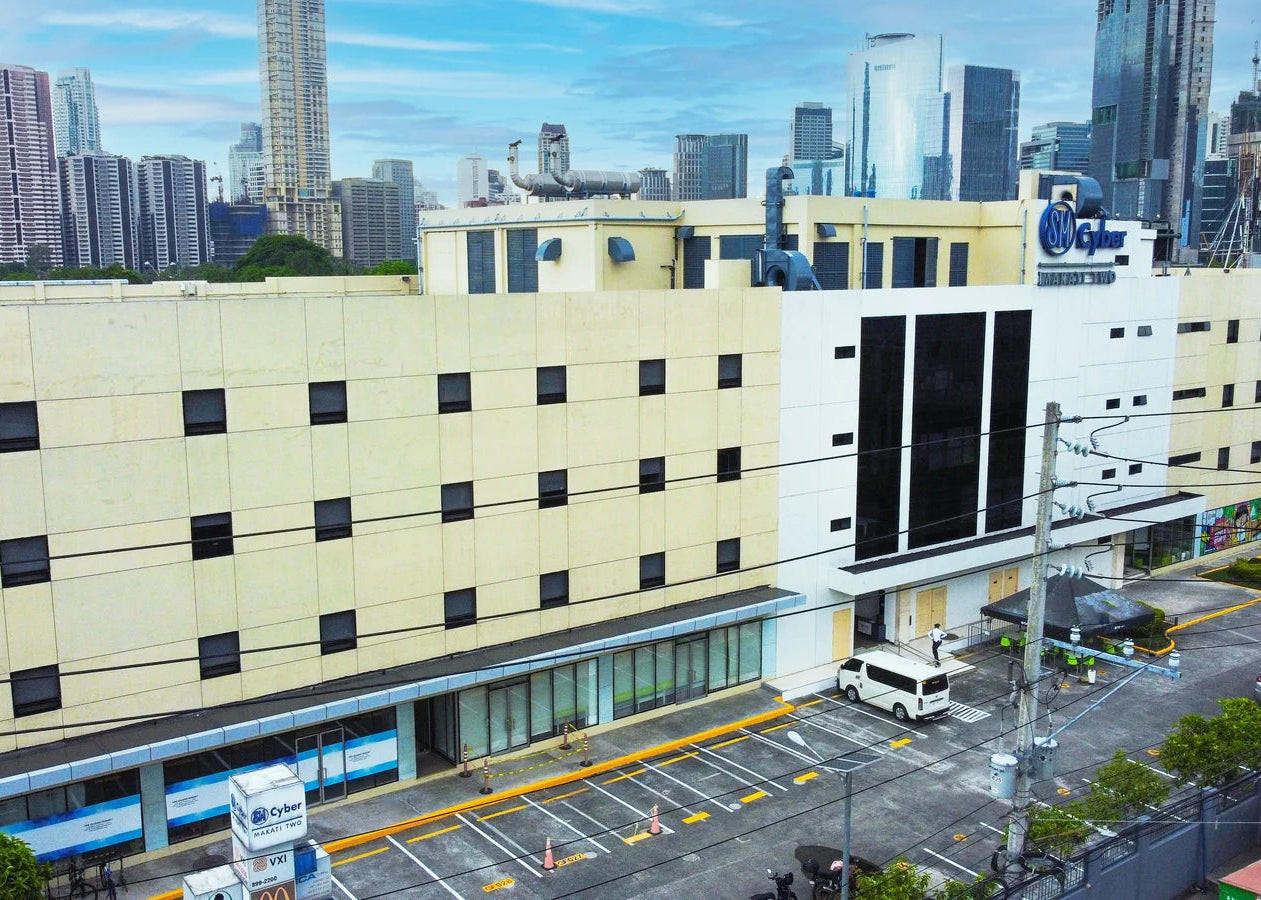 Aerial view of a large beige and white hotel building with a blue Hilton logo, situated in a city with tall skyscrapers in the background.