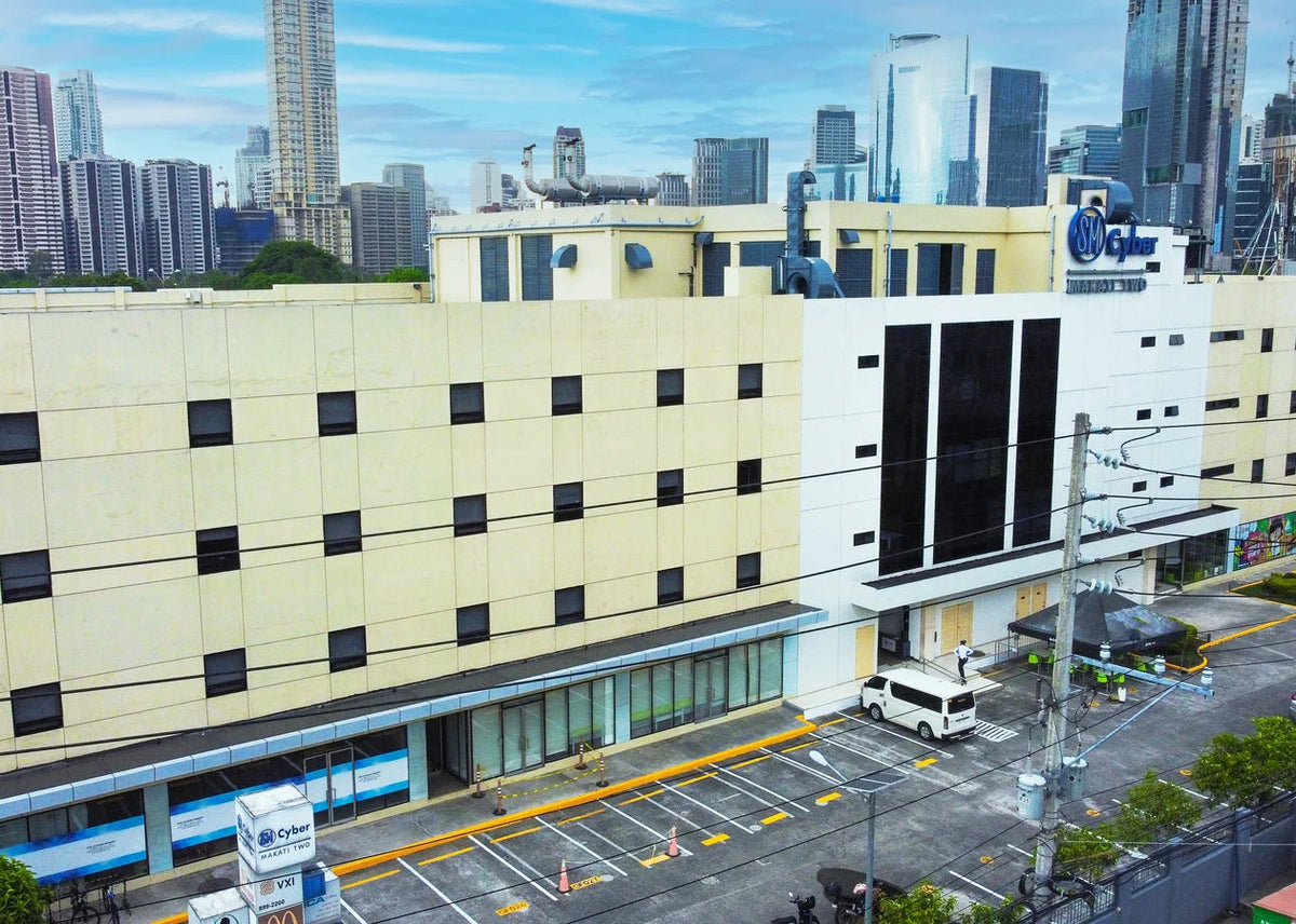 Aerial view of a large beige and white hotel building with a blue Hilton logo, situated in a city with tall skyscrapers in the background.