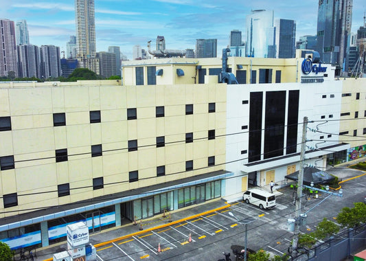 Aerial view of a large beige and white hotel building with a blue Hilton logo, situated in a city with tall skyscrapers in the background.